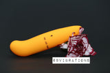 A Mini Dolphin Vibrator in a sleek, orange curve with the "69 Vibrations" logo beside it rests against a maroon and white carnation flower on a black background. This vibrator includes an on/off switch labeled on its side. Discover this and more at our sex toys shop in Nairobi.