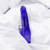 The Crystal Climbing Rabbit Vibrator by 69Vibrations, a purple, translucent sex toy with a phallic design, dual stimulators, textured ridges, and a clear tip, lies on white sheets. It offers 69 vibrations for enhanced pleasure.